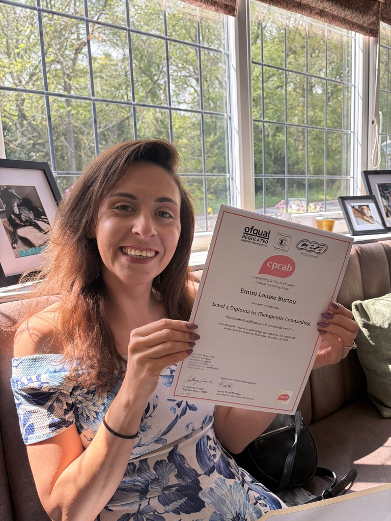 Emmi smiling and holding up her CPCAB Level 4 Diploma in Therapeutic Counselling certificate
